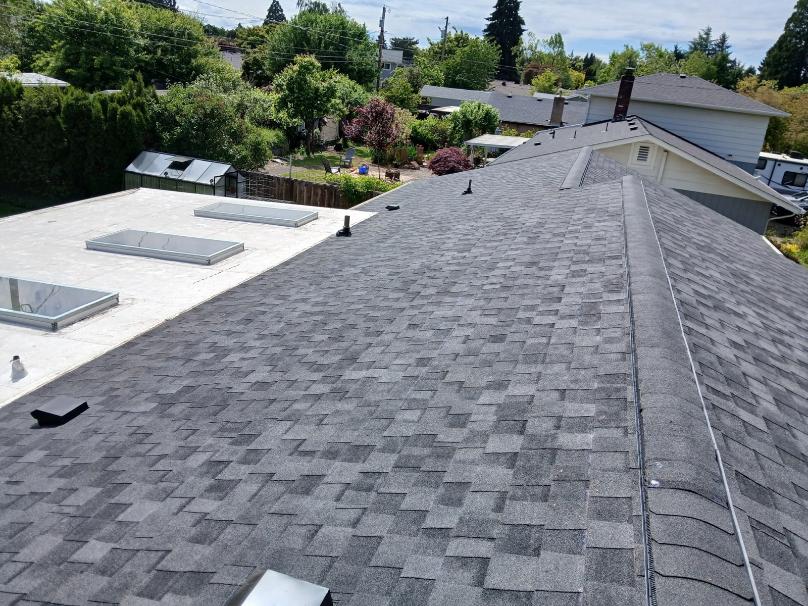 The completed architectural asphalt shingle roof on the ranch home under a clear sky.